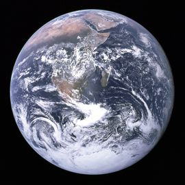 A planetary disk of white cloud formations, brown and green land masses, and dark blue oceans against a black background. The Arabian peninsula, Africa and Madagascar lie in the upper half of the disk, while Antarctica is at the bottom.